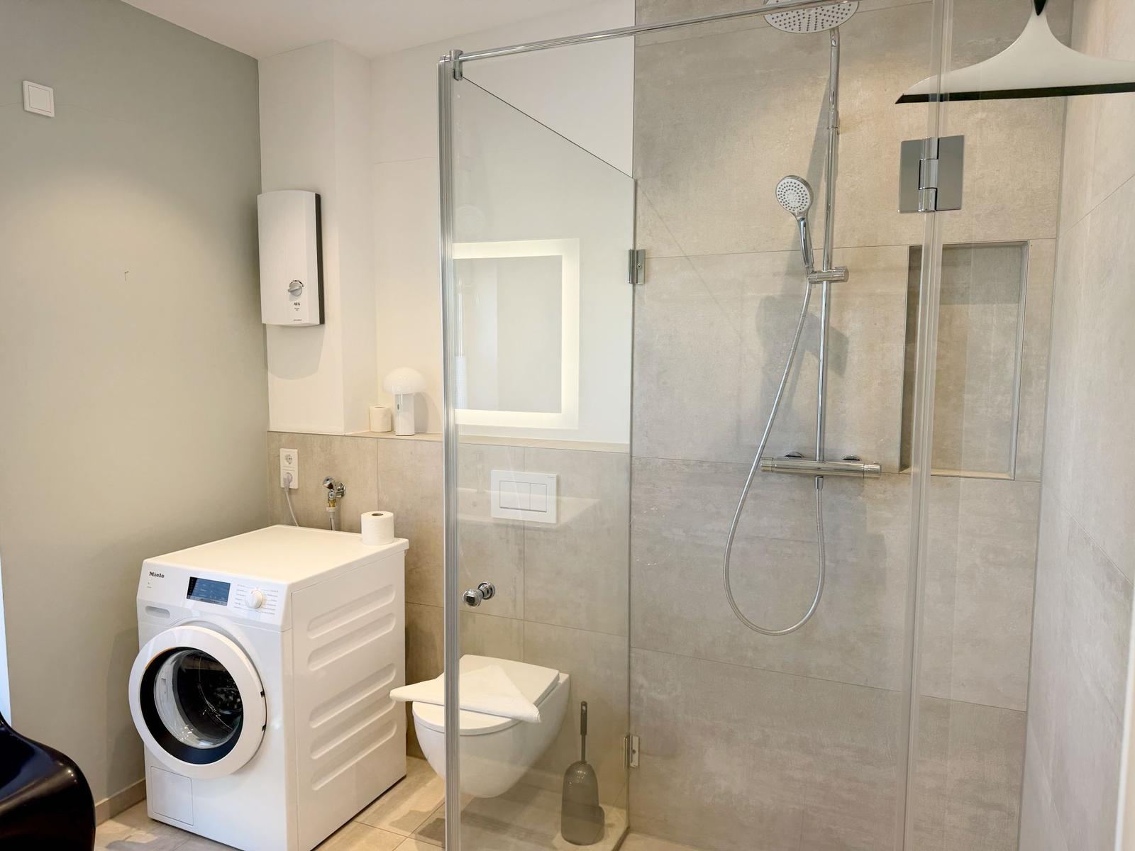 Dusche mit Duschbrause, Toilette und Waschmaschine im Badezimmer.
