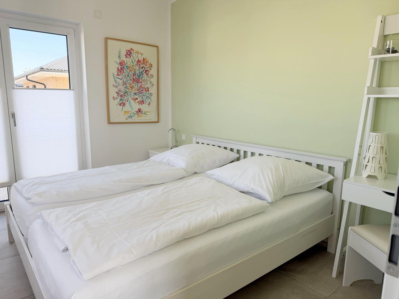 Schlafzimmer mit weißem Bett, Fenster und Wandbild.
