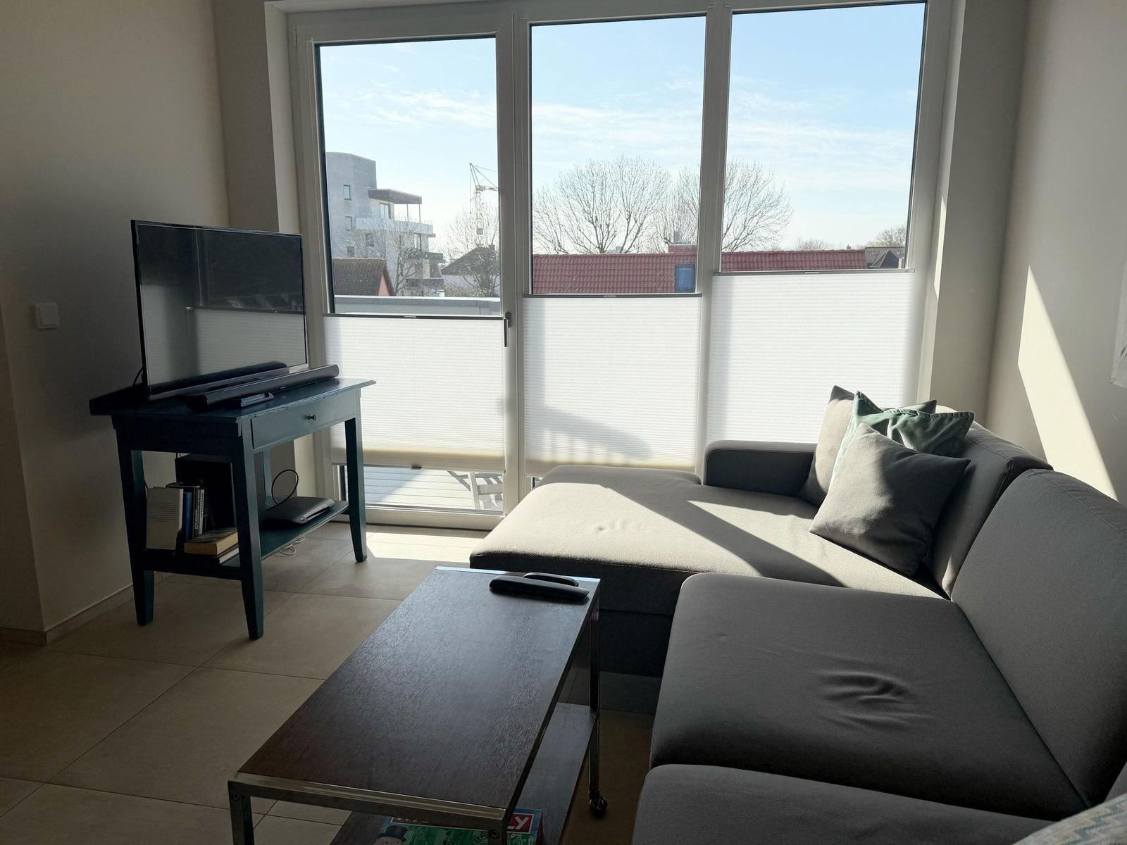 Wohnzimmer mit Sofa, Fernseher und großem Fenster mit Blick auf die Straße.