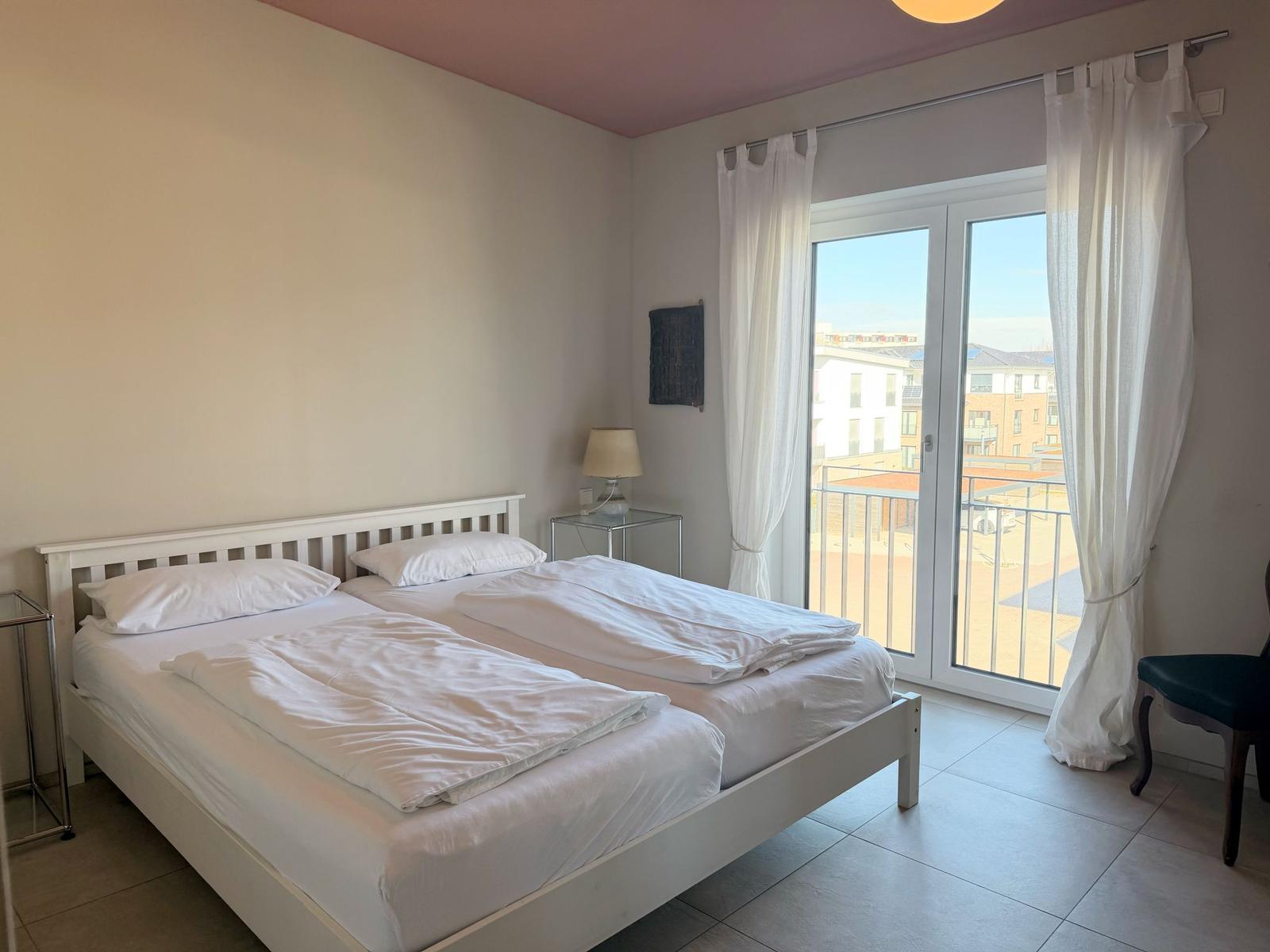 Schlafzimmer mit Doppelbett, Balkon und weißen Vorhängen.