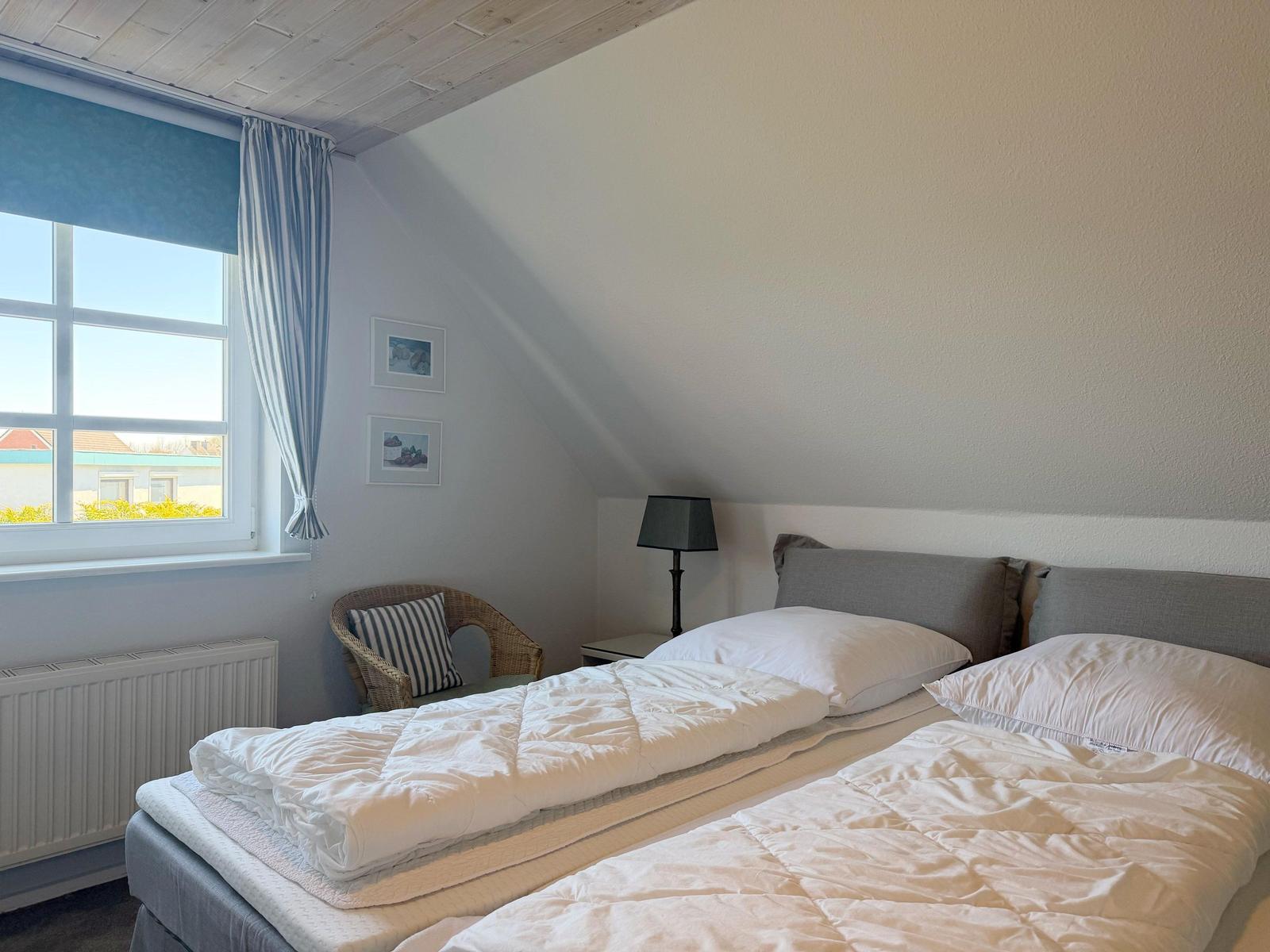 Zimmer mit Doppelbett, Fenster und Stuhl unter schrägem Dach