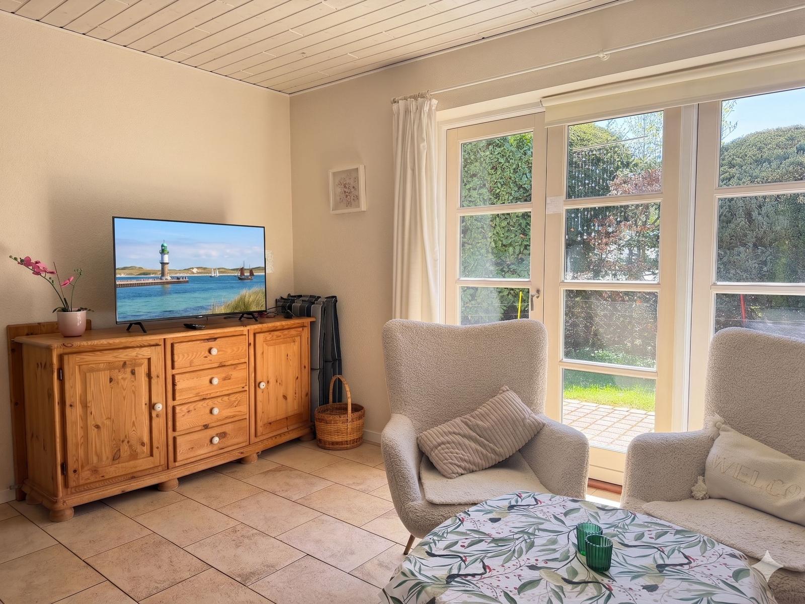 Wohnzimmer mit Fernseher, Sitzgelegenheiten und Blick auf den Garten.