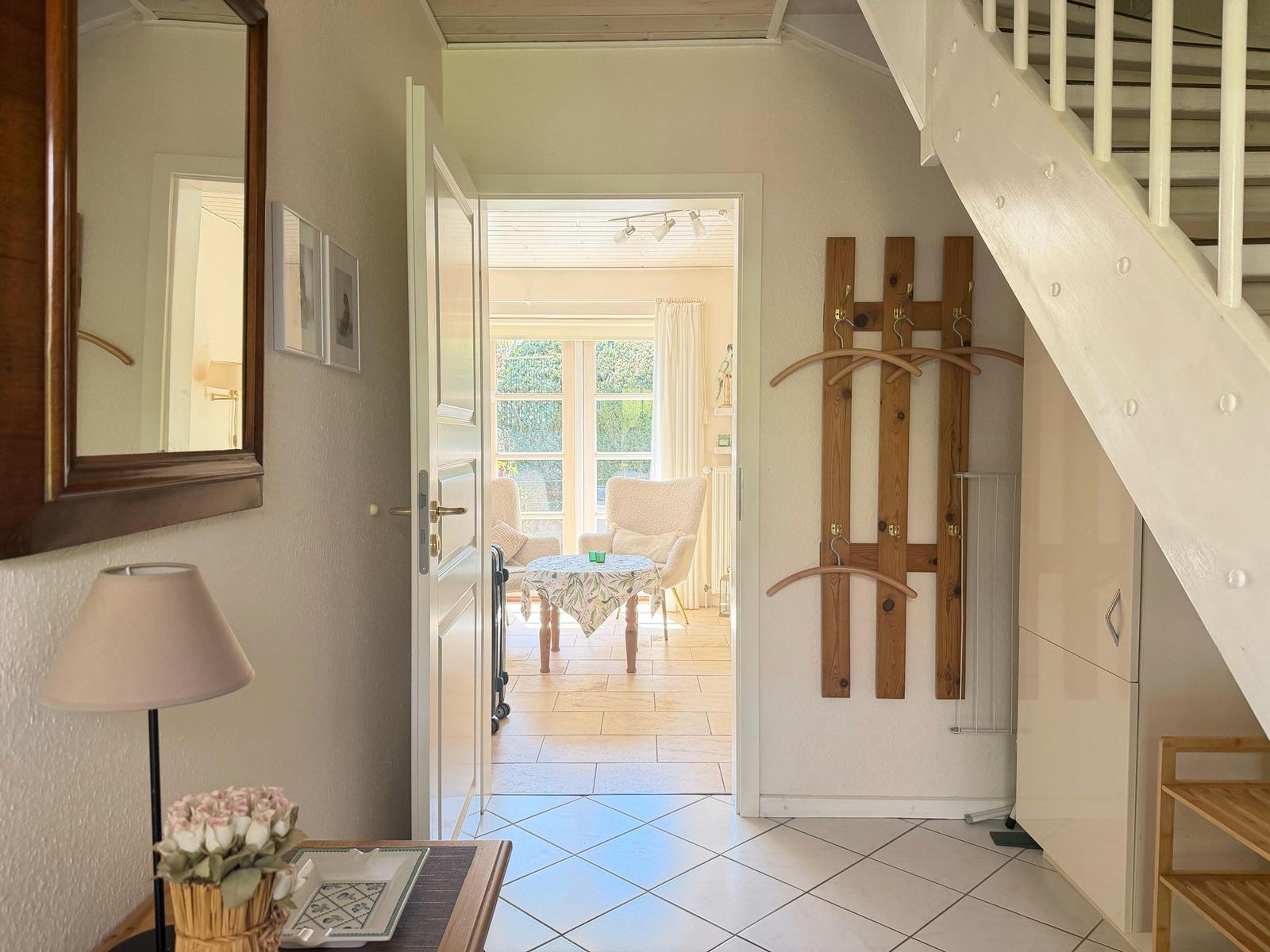 Eingangsbereich mit Holzgarderobe, Treppe und Blick in Wohnbereich mit Tisch und Stühlen.
