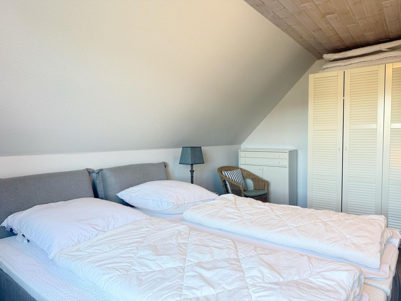Zimmer mit Doppelbett, Schrank und Sessel unter schrägem Dach