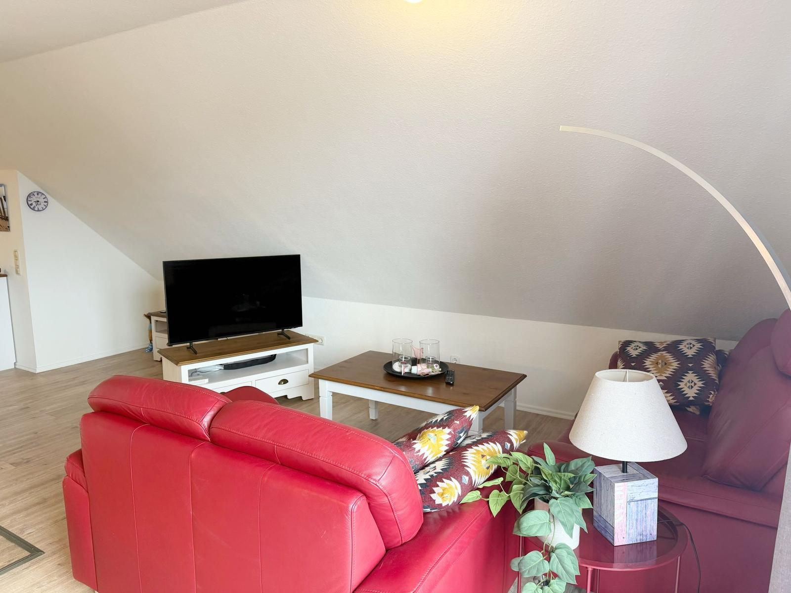 Wohnzimmer mit rotem Sofa, Fernseher und Tisch unter schrägem Dach