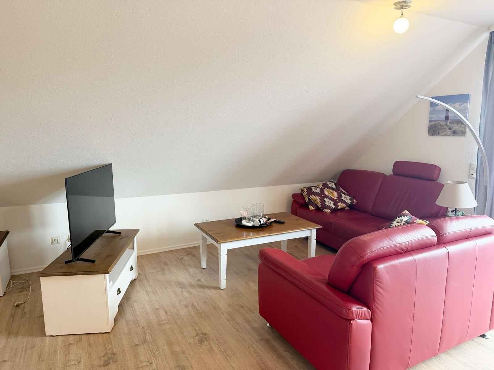 Ein Wohnzimmer mit rotem Sofa, Holztisch und Fernseher auf einem weißen Schrank.