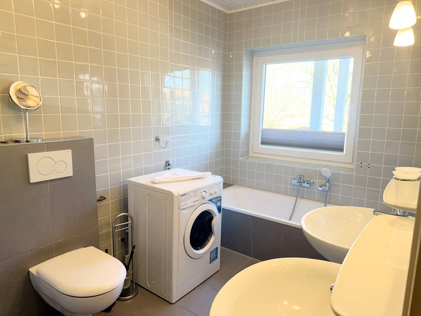 Badezimmer mit Badewanne, Waschmaschine, Toilette und Waschbecken.