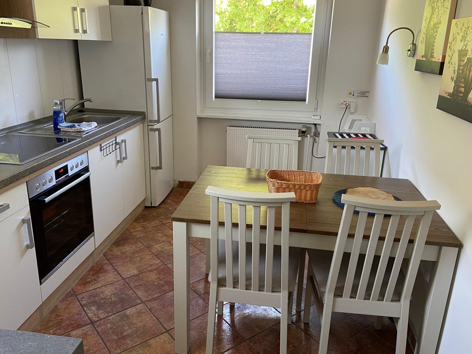 Küche mit Essbereich, Holztisch, vier Stühle, Kühlschrank und Fenster.