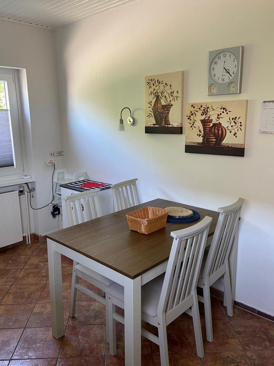 Esszimmer mit Holztisch, weißen Stühlen, Wandbildern und Uhr.