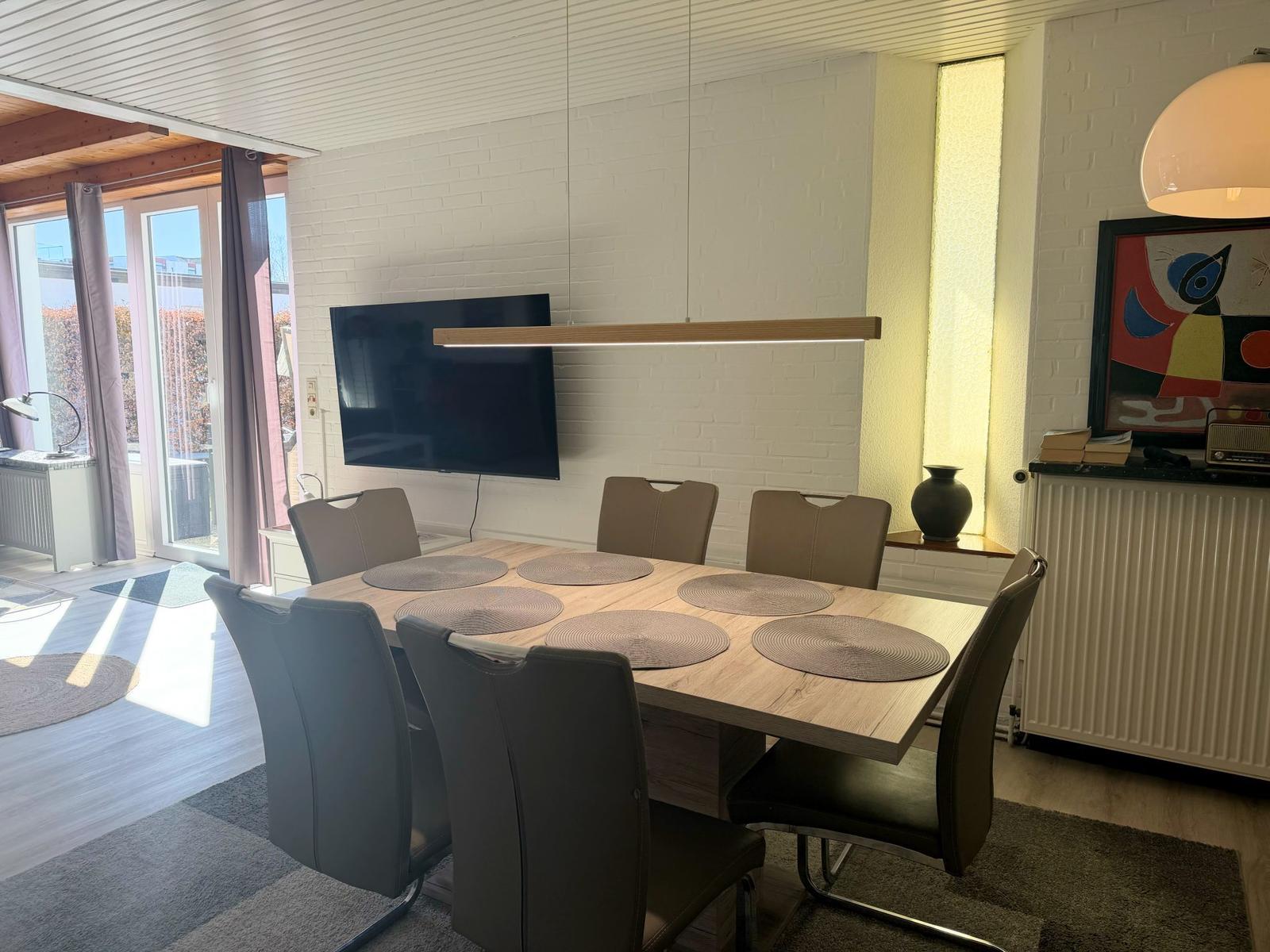 Esszimmer mit Holztisch, sechs Stühlen und Fernseher an der Wand.