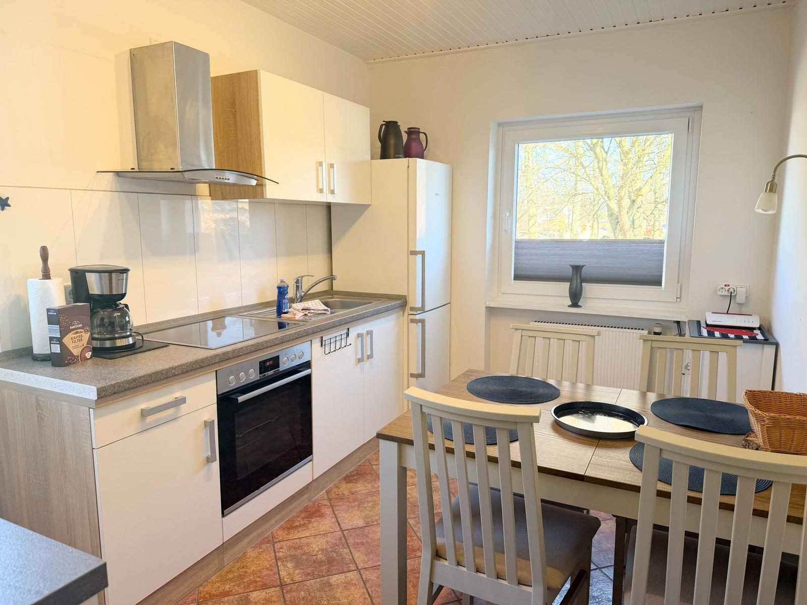 Küche mit Essbereich, weiße Schränke, Kühlschrank und Fenster mit Blick.