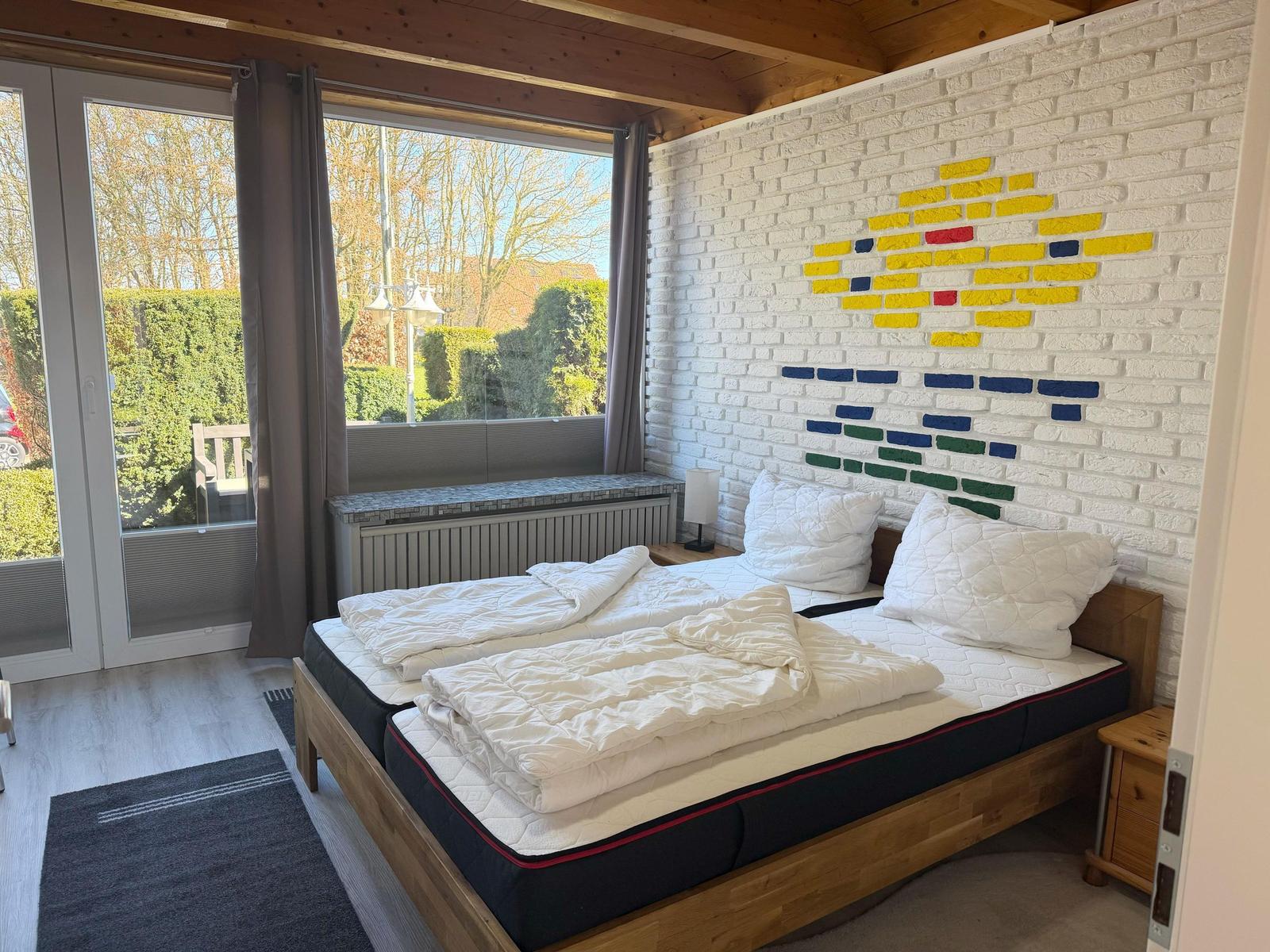 Schlafzimmer mit Doppelbett, weißer Ziegelwand und Blick auf den Garten.