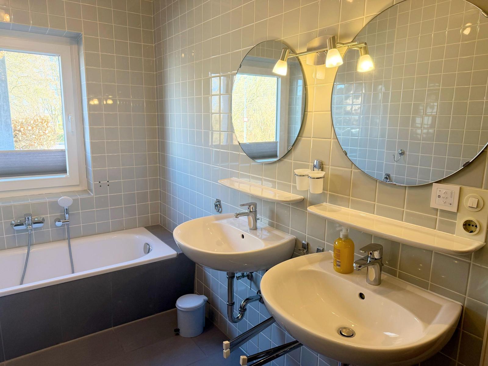 Badezimmer mit Badewanne, zwei Waschbecken und runden Spiegeln an der Wand.