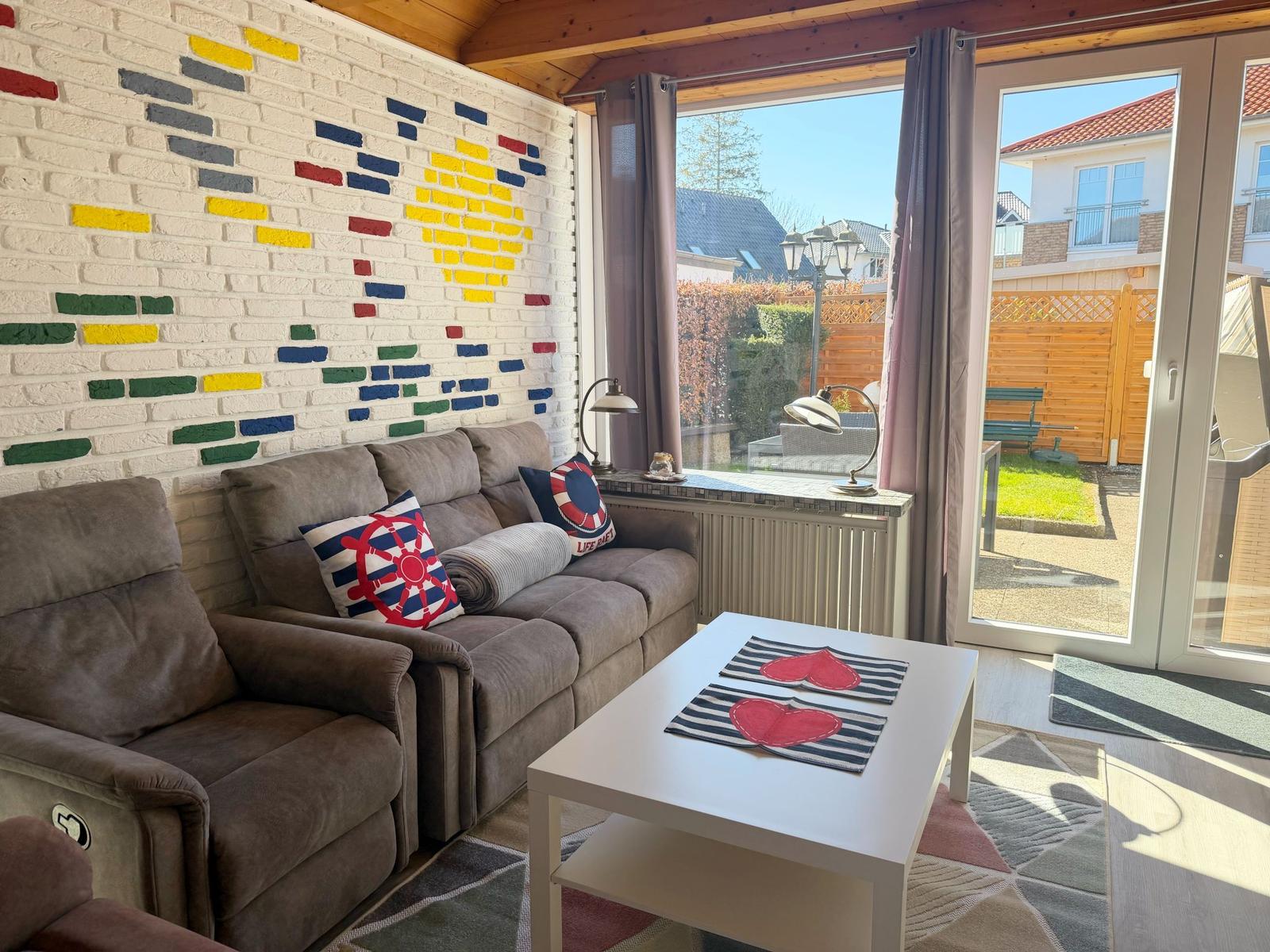 Wohnzimmer mit Sofa, Tisch und Fenster zur Terrasse.