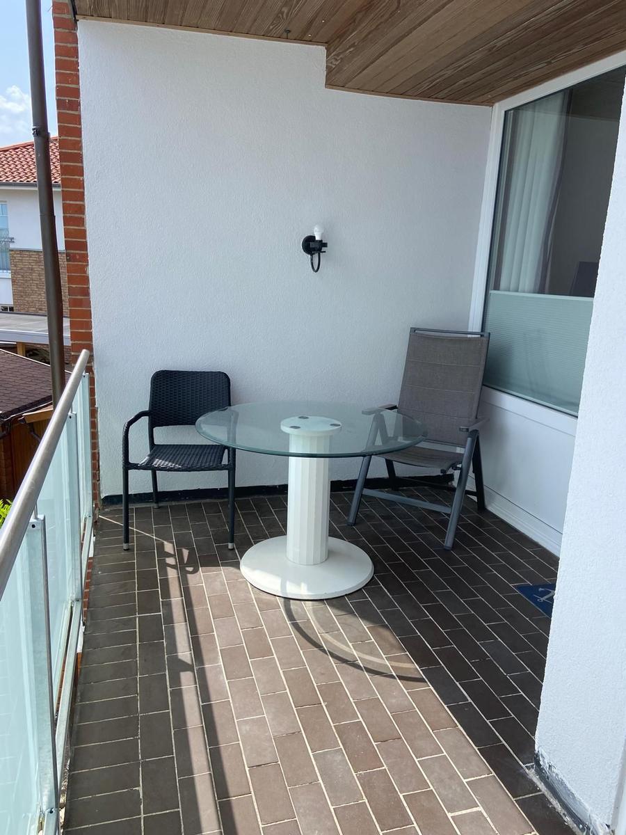 Terrasse mit Glas-Tisch, zwei Stühlen und Holzdecke. Fliesenboden und Glastür.