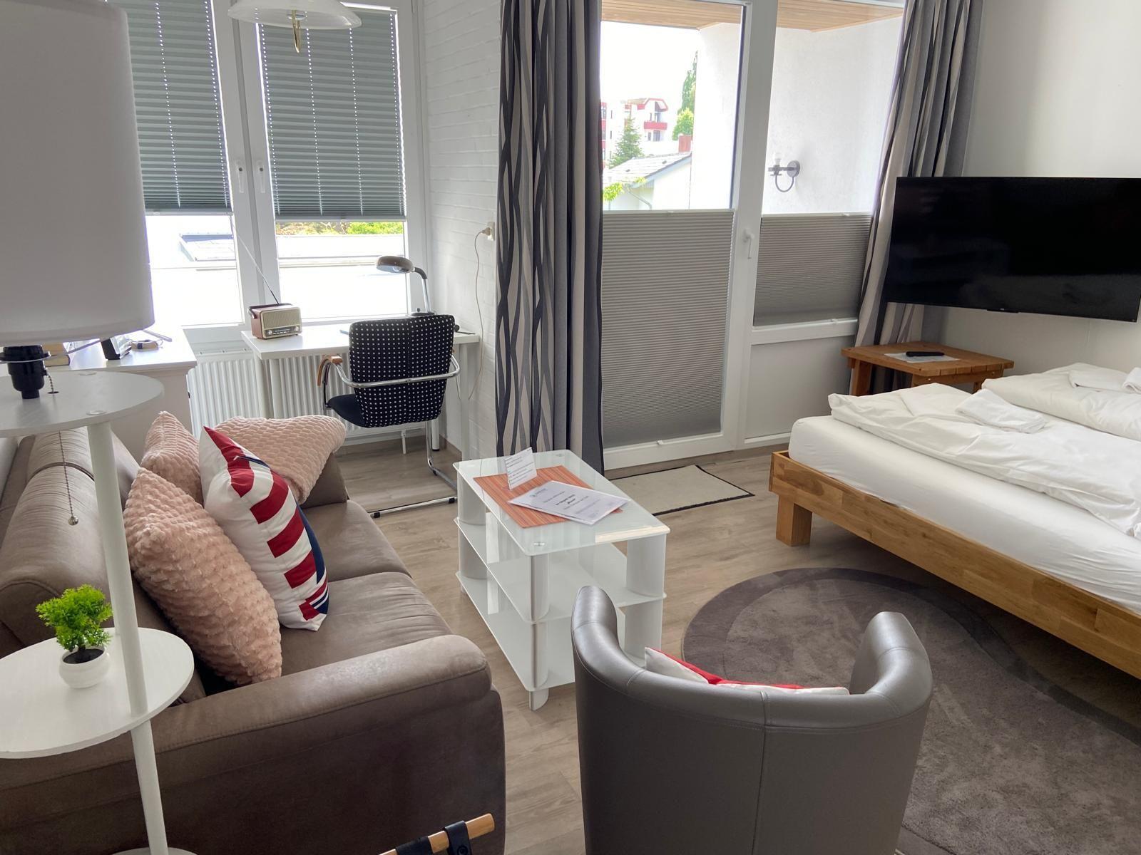 Ein Zimmer mit Bett, Sofa, Fernseher und Balkon. Möbel sind modern und funktional.