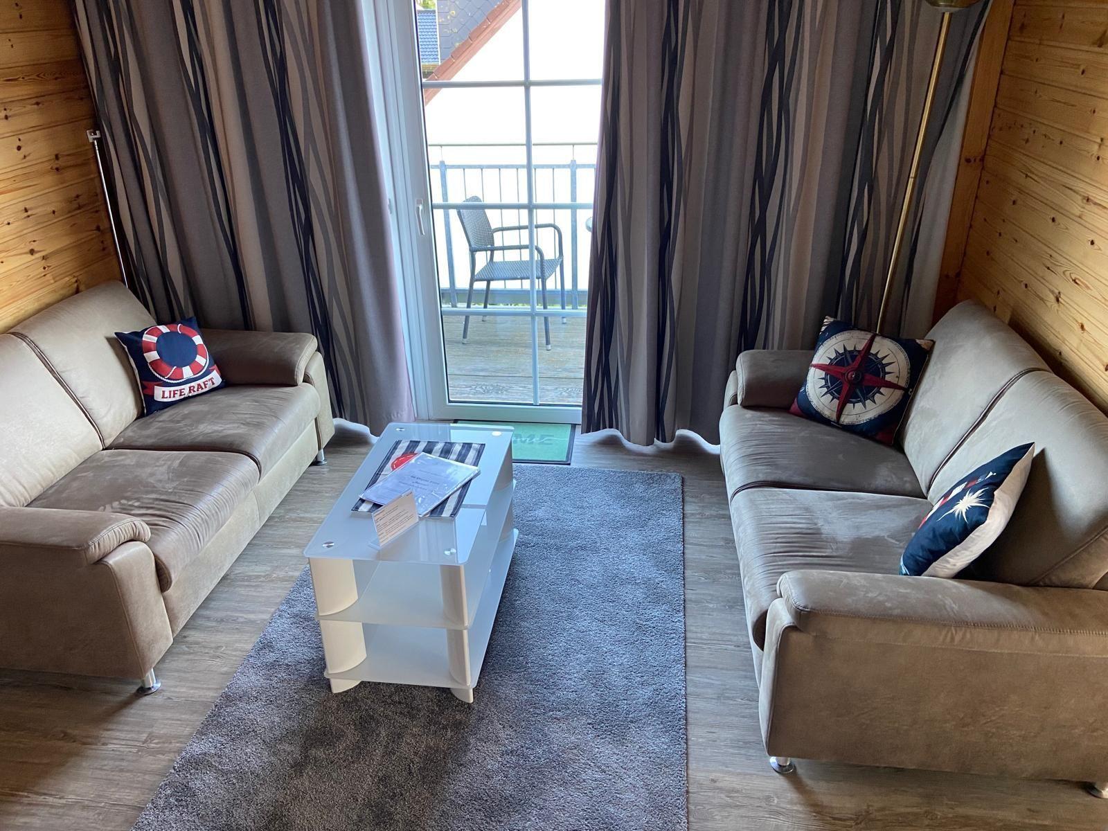 Two sofas with cushions surround a white coffee table. A balcony is accessible through the glass door.