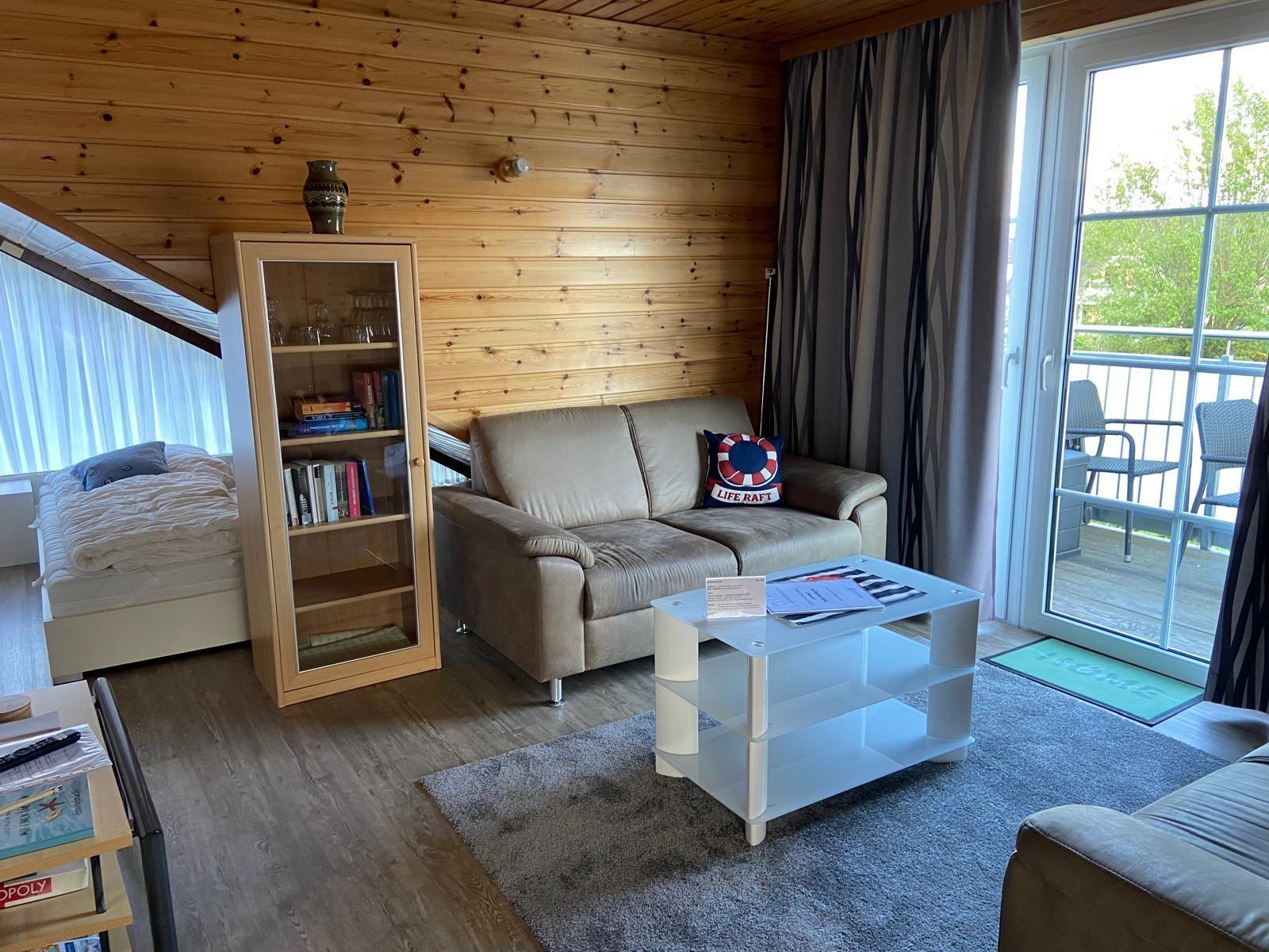 Living room with sofa, coffee table, and bookcase. Balcony with seating.