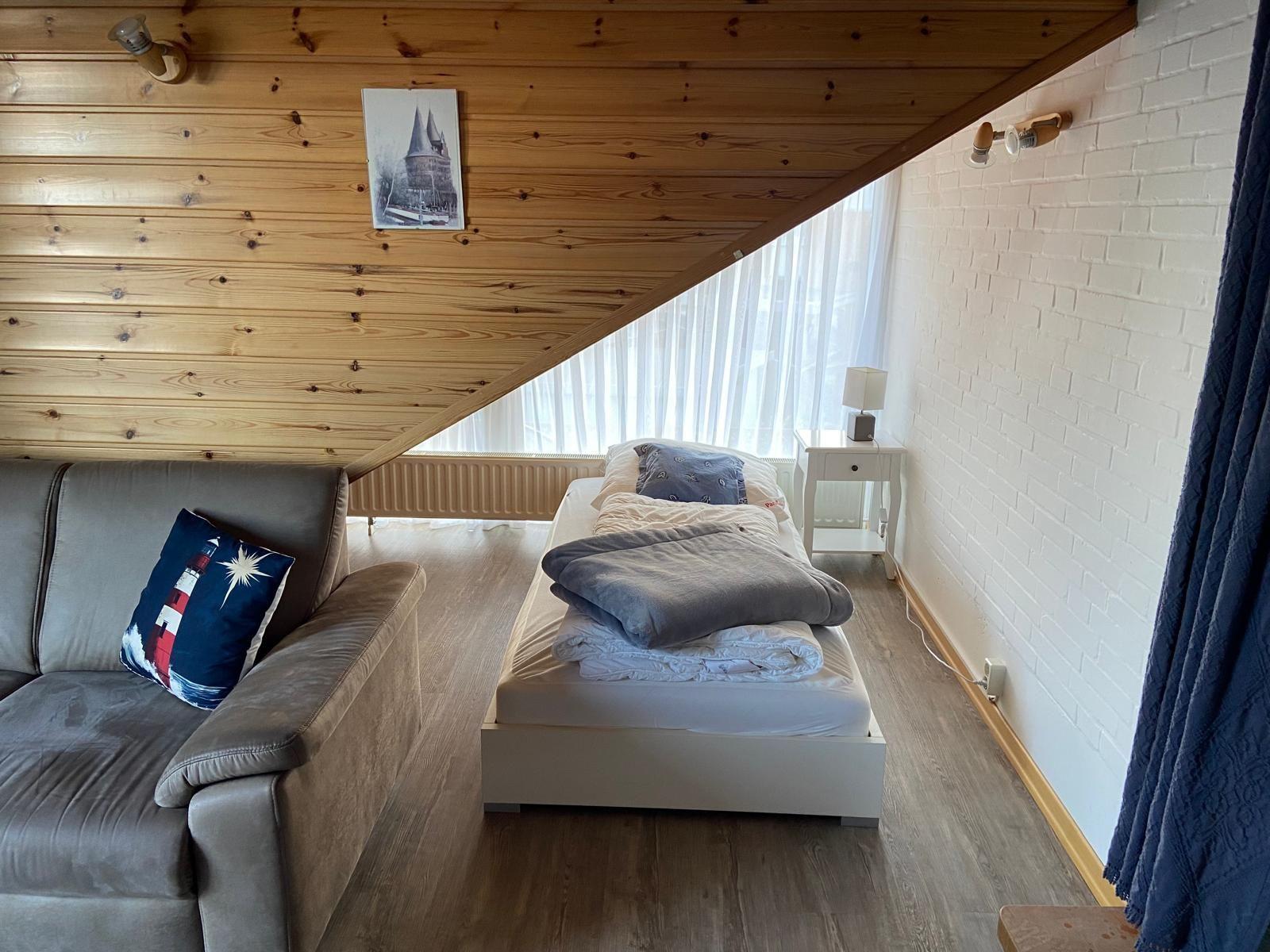 Room with bed, sofa, and wooden ceiling. Window with curtains and white wall.