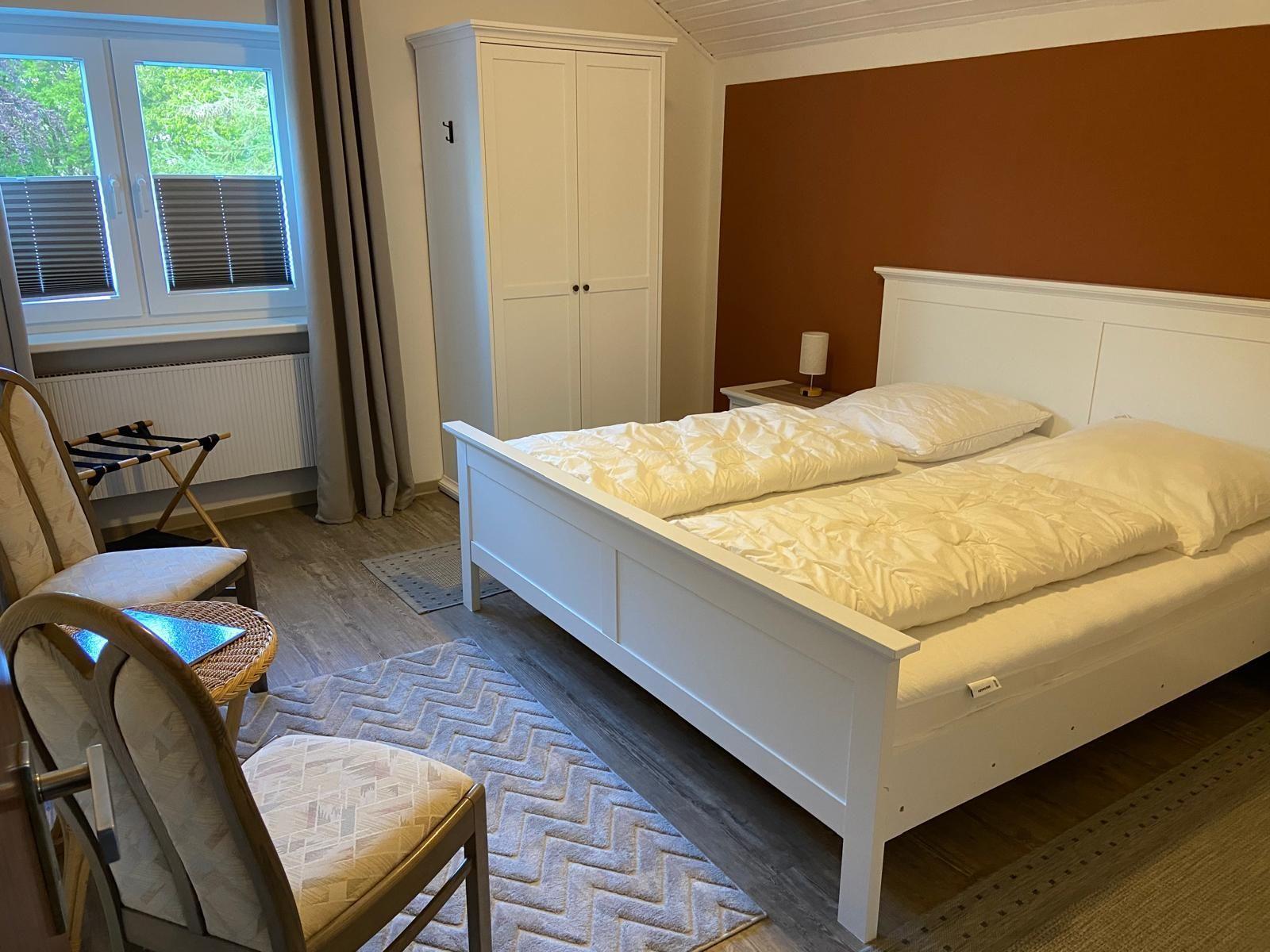 Bedroom with white bed, wardrobe, and window with view of greenery.