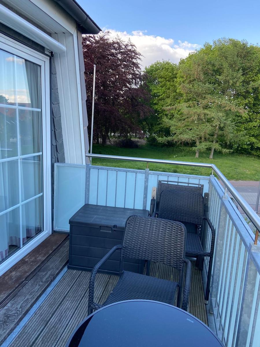 Terrace with two chairs, table, and storage box. View of green trees and lawn.