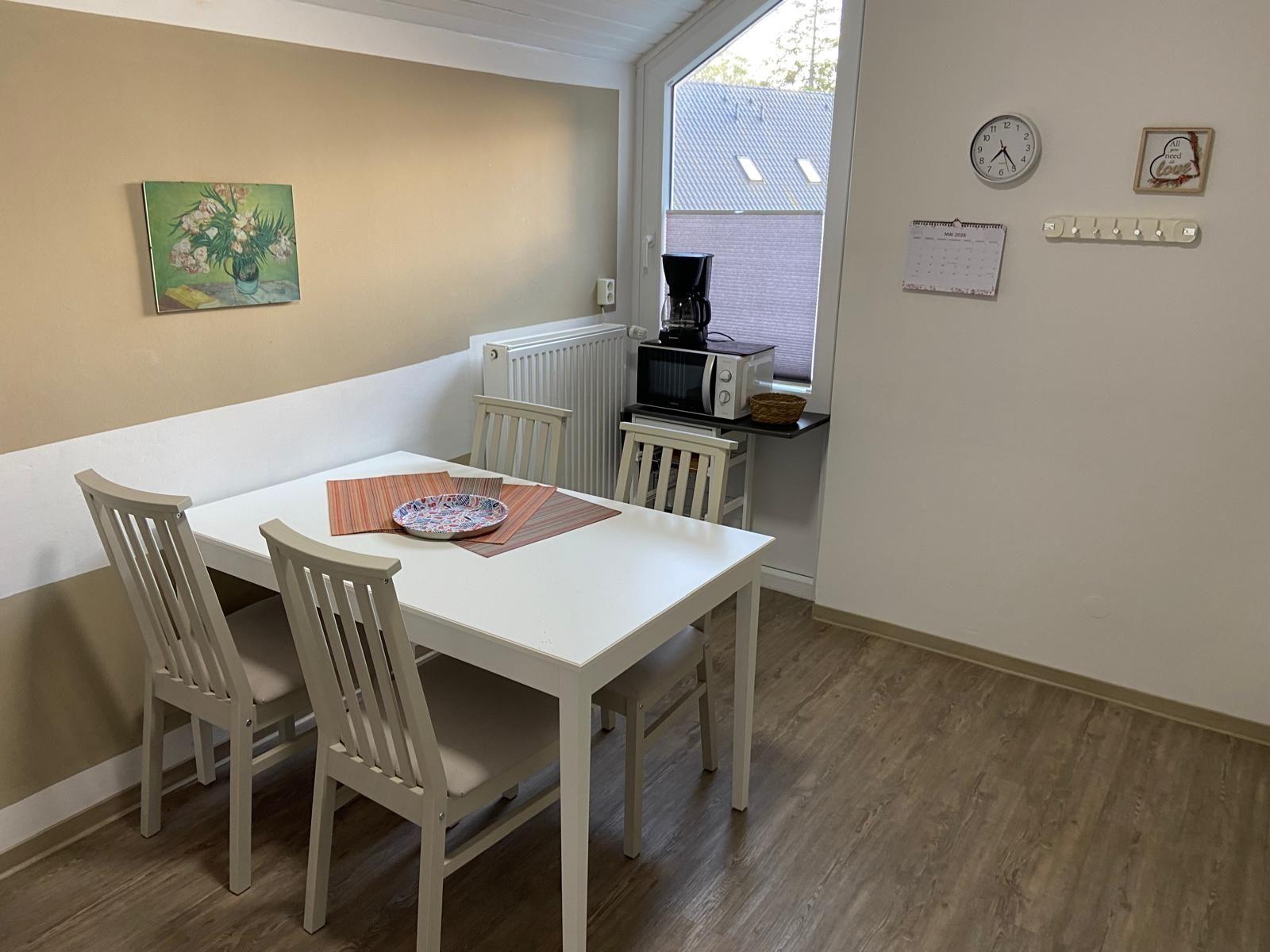 Dining room with white table, four chairs, and kitchenette with microwave and coffee maker.