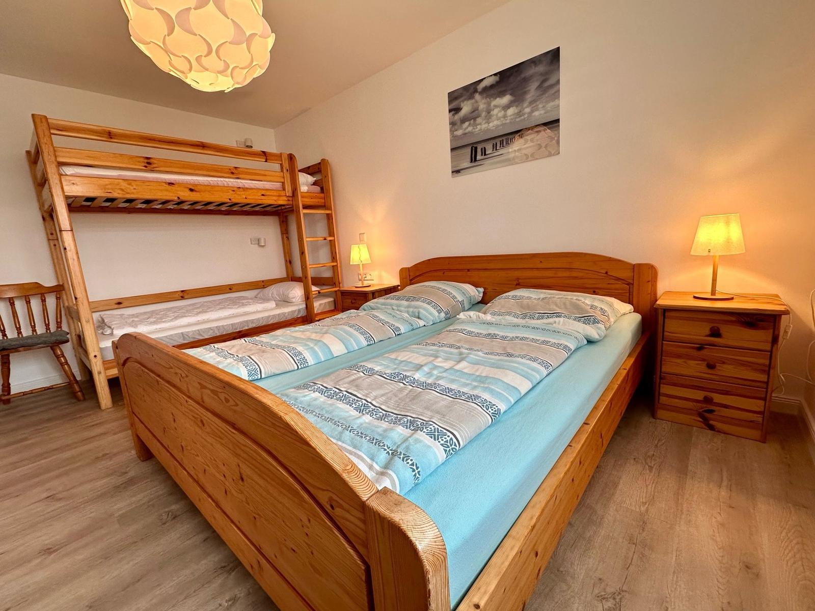 Zimmer mit Doppelbett, Etagenbett und Nachttisch mit Lampe.