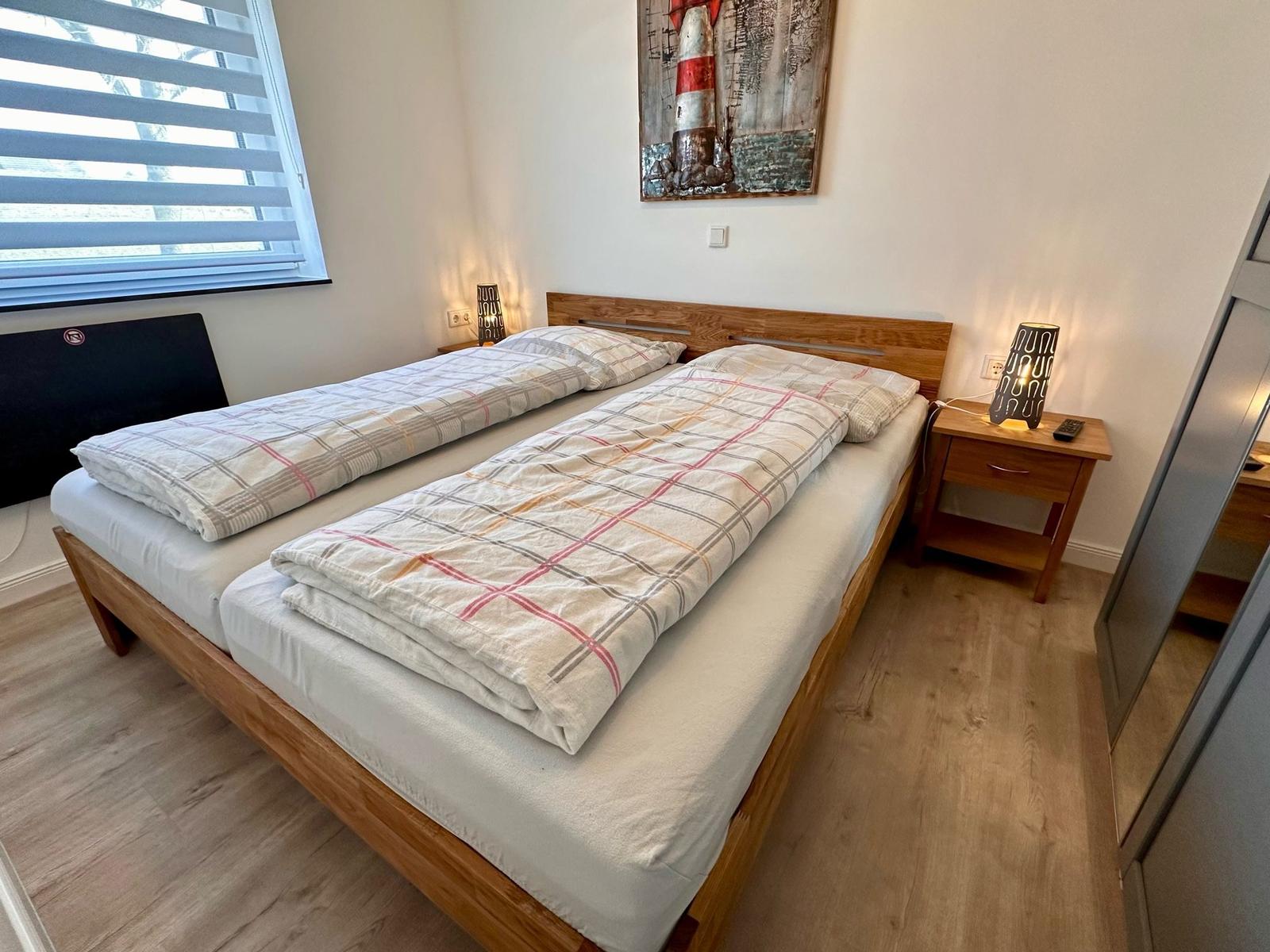 Schlafzimmer mit Doppelbett, Nachttisch und Fenster mit Jalousie.