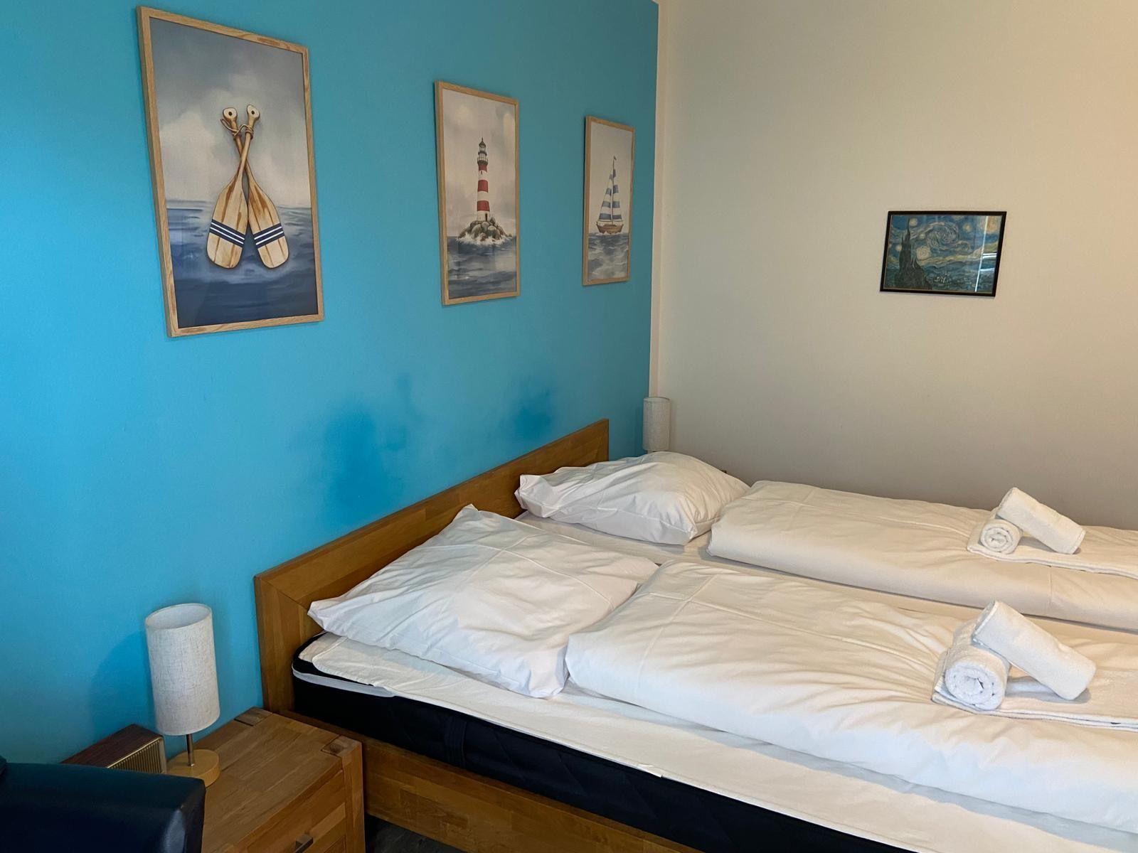 Zwei Betten mit weißen Bettwäschen, blaue Wand mit Seemotiven, Nachttisch und Lampe.