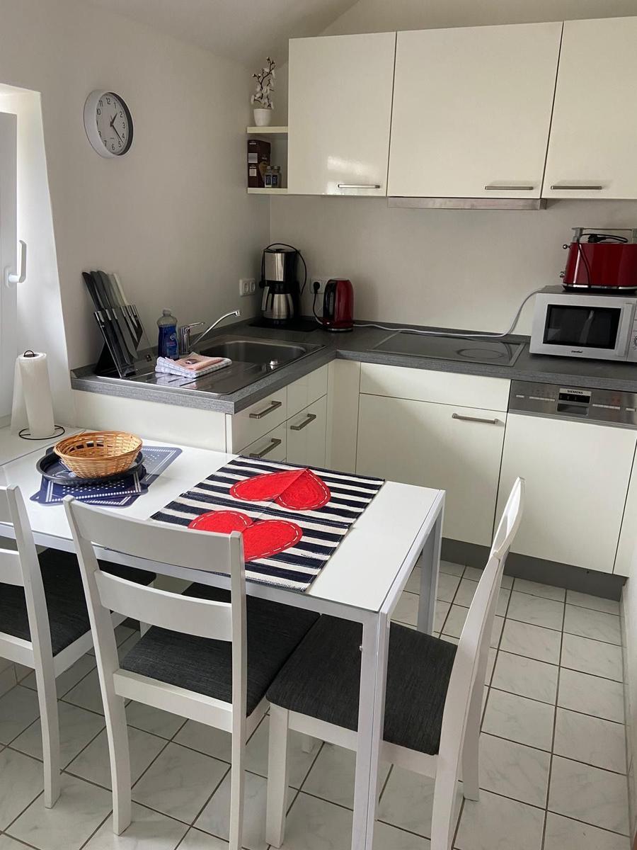 Küche mit Essbereich, weiße Schränke, Tisch mit Stühlen und Küchengeräten.