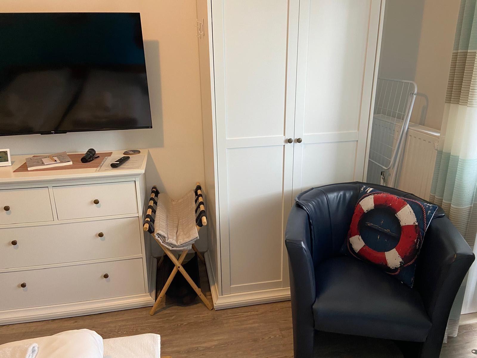 Schlafzimmer mit TV, Kleiderschrank und Sessel mit Rettungsringkissen.