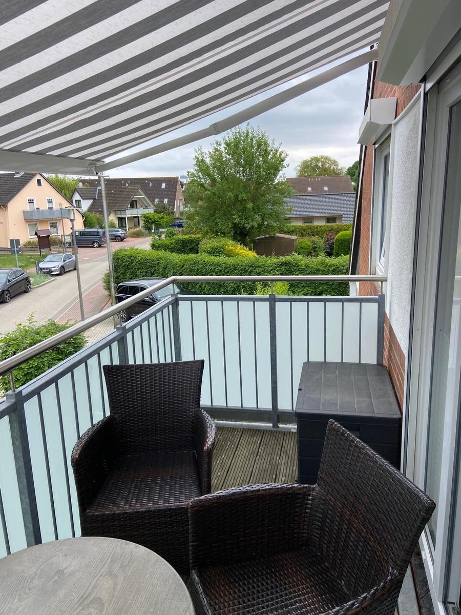 Terrasse mit Schutzmarkise, zwei Stühlen und Tisch. Blick auf Straße und Grünanlagen.