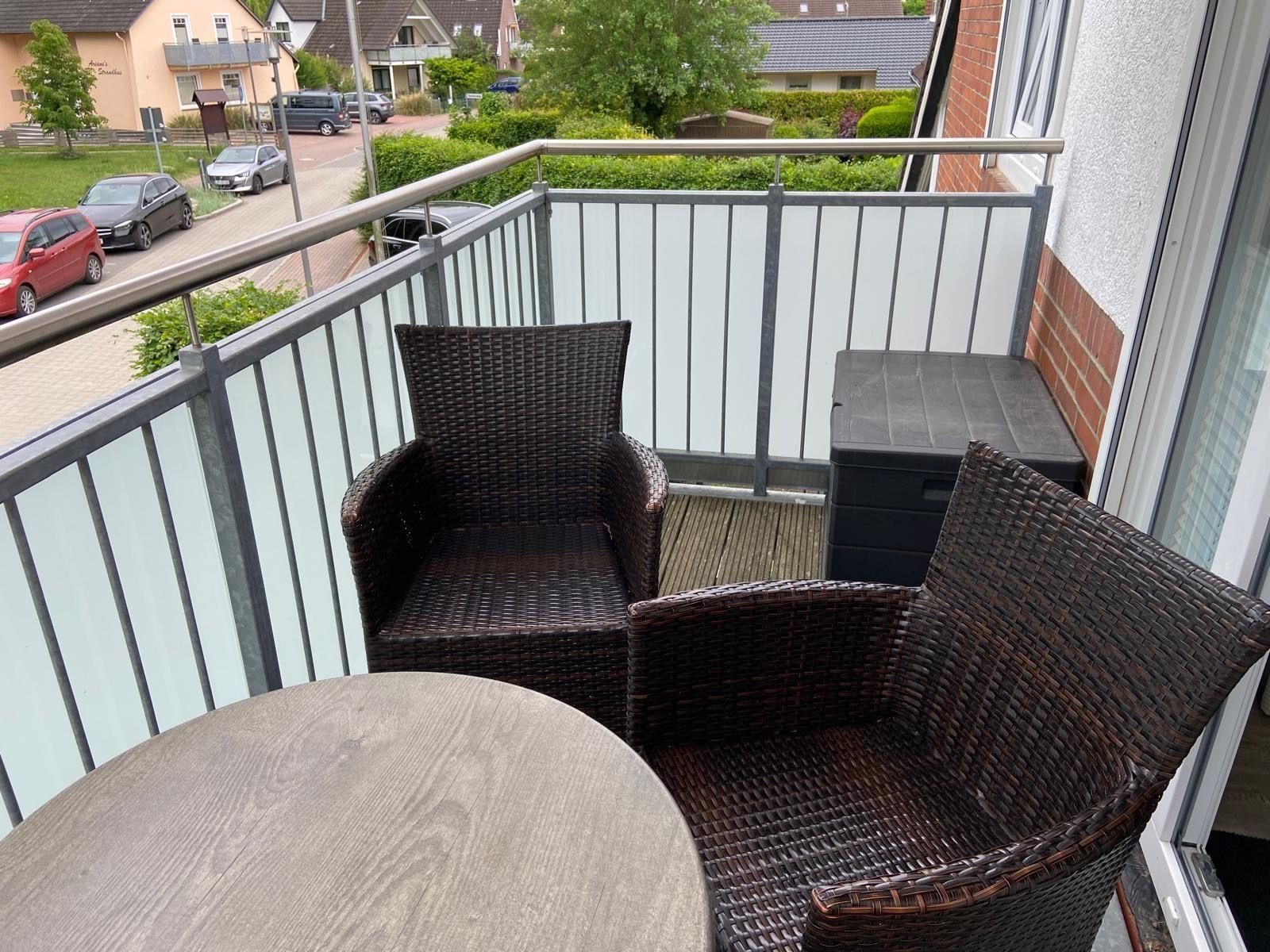 Balkon mit zwei Stühlen und Tisch. Blick auf Straße und Grünflächen.