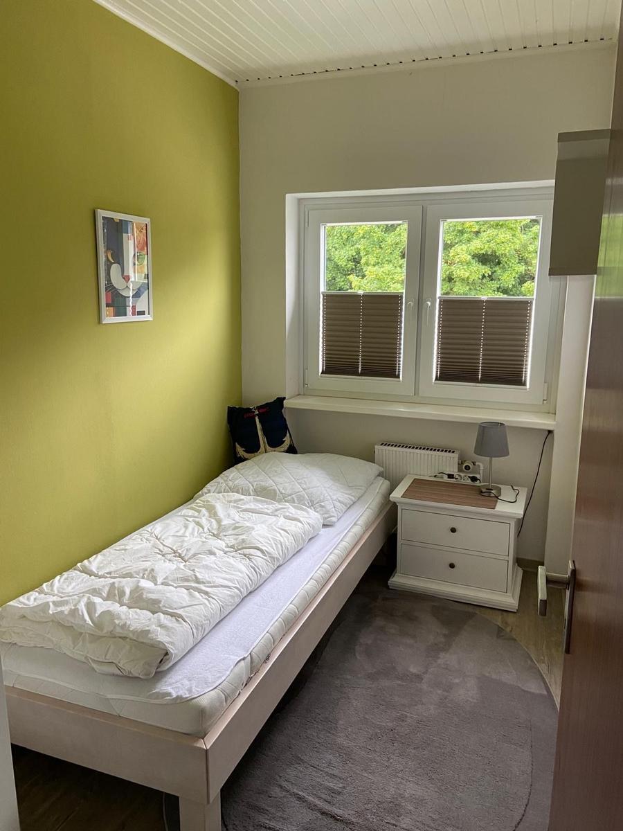 Ein Schlafzimmer mit einem Bett, einem Nachttisch und einem Fenster mit Blick auf Bäume.