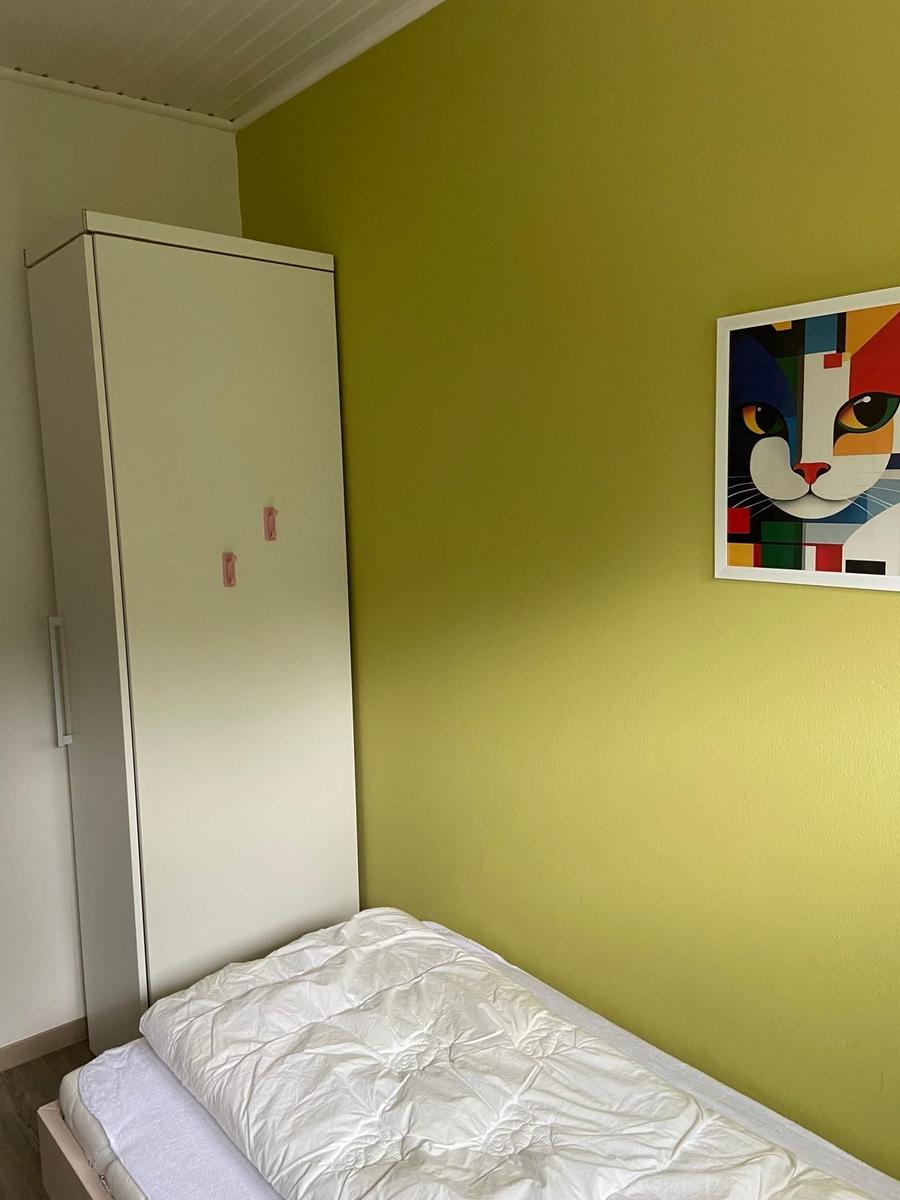 Schlafzimmer mit Bett, Kleiderschrank und Wandbild mit Katzenmotiv.