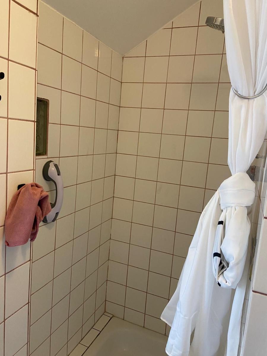 Dusche mit weißen Fliesen, Duschvorhang und Handtuchhalter.