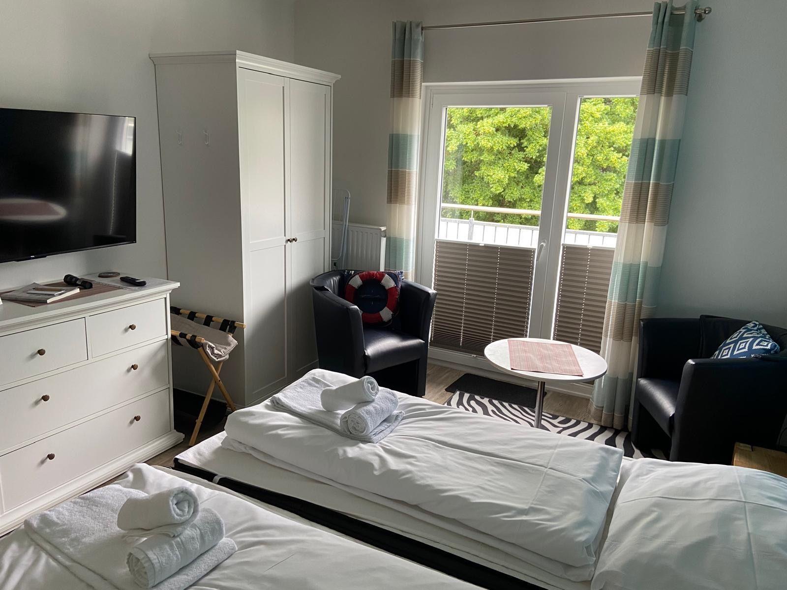 Zwei Betten, TV, Schrank und Balkon mit Blick auf Bäume.