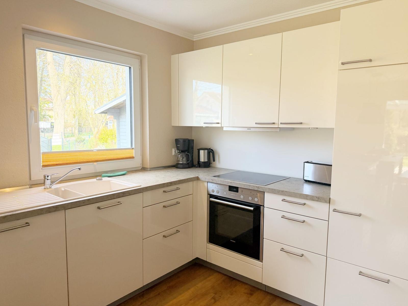 Küche mit weißen Schränken, Fenster, Spüle und Herd.
