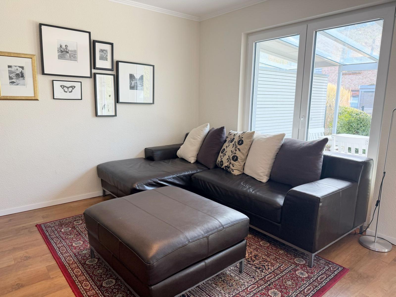 Ein Wohnzimmer mit einem schwarzen Ledersofa und einem passenden Hocker auf einem Teppich.