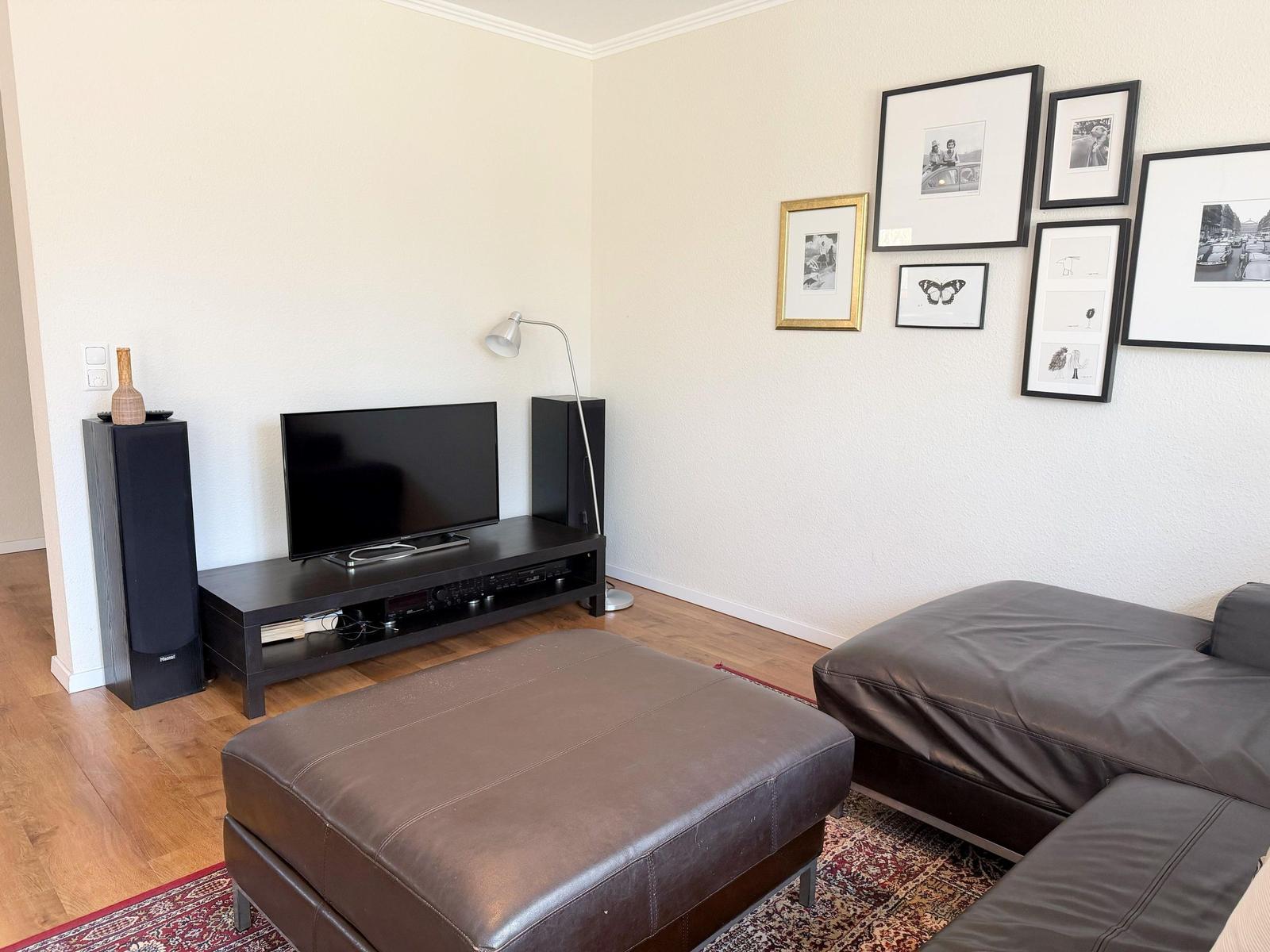 Wohnzimmer mit Ledersofa, Fernseher und Wandbildern.