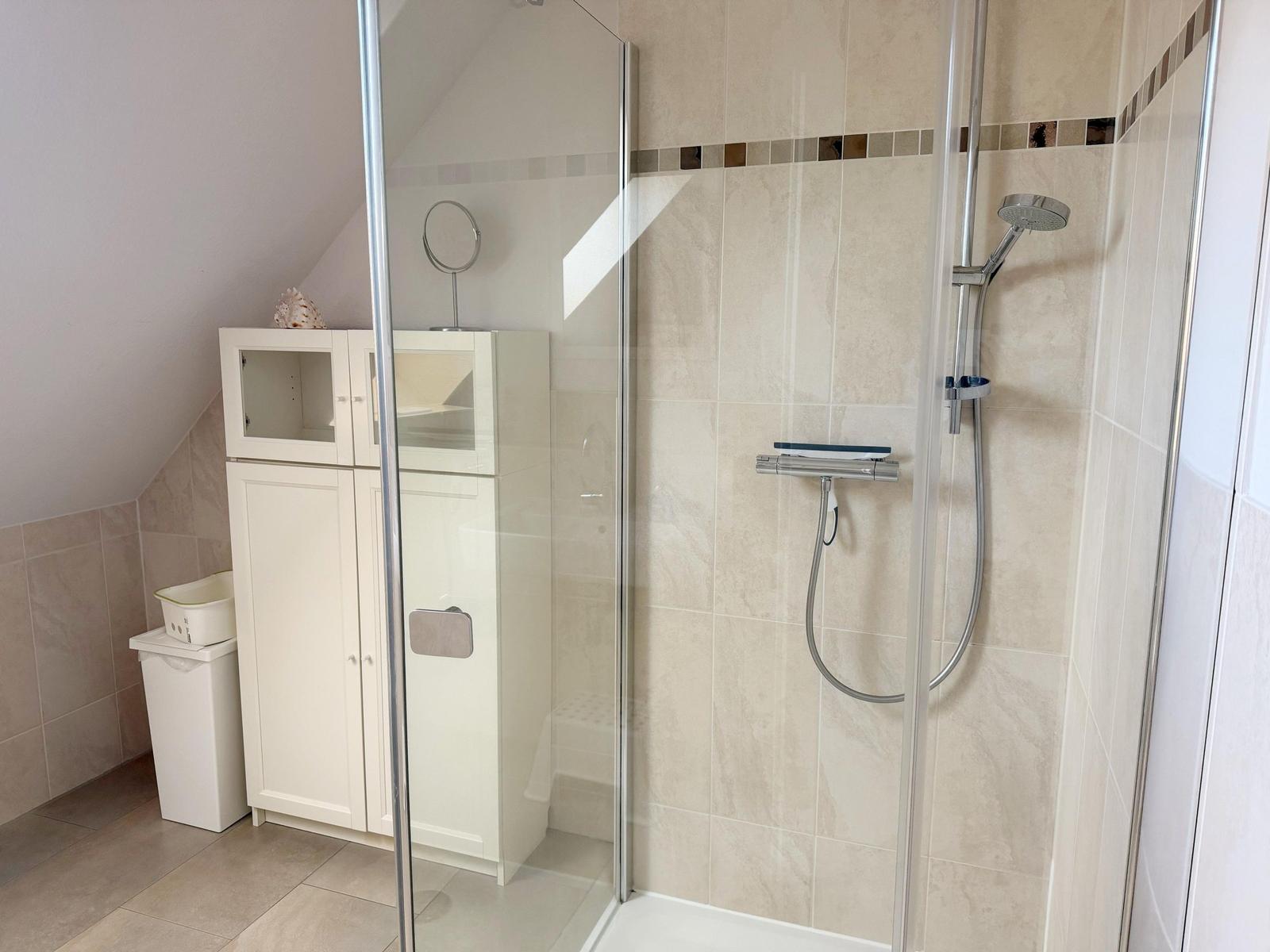 Dusche mit Glaswand, weiße Schränke und Mosaikfliesen an der Wand.