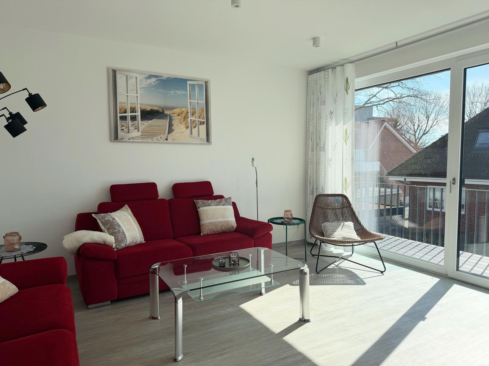 Ein Wohnzimmer mit rotem Sofa, Glas-Tisch und Blick auf Balkon.