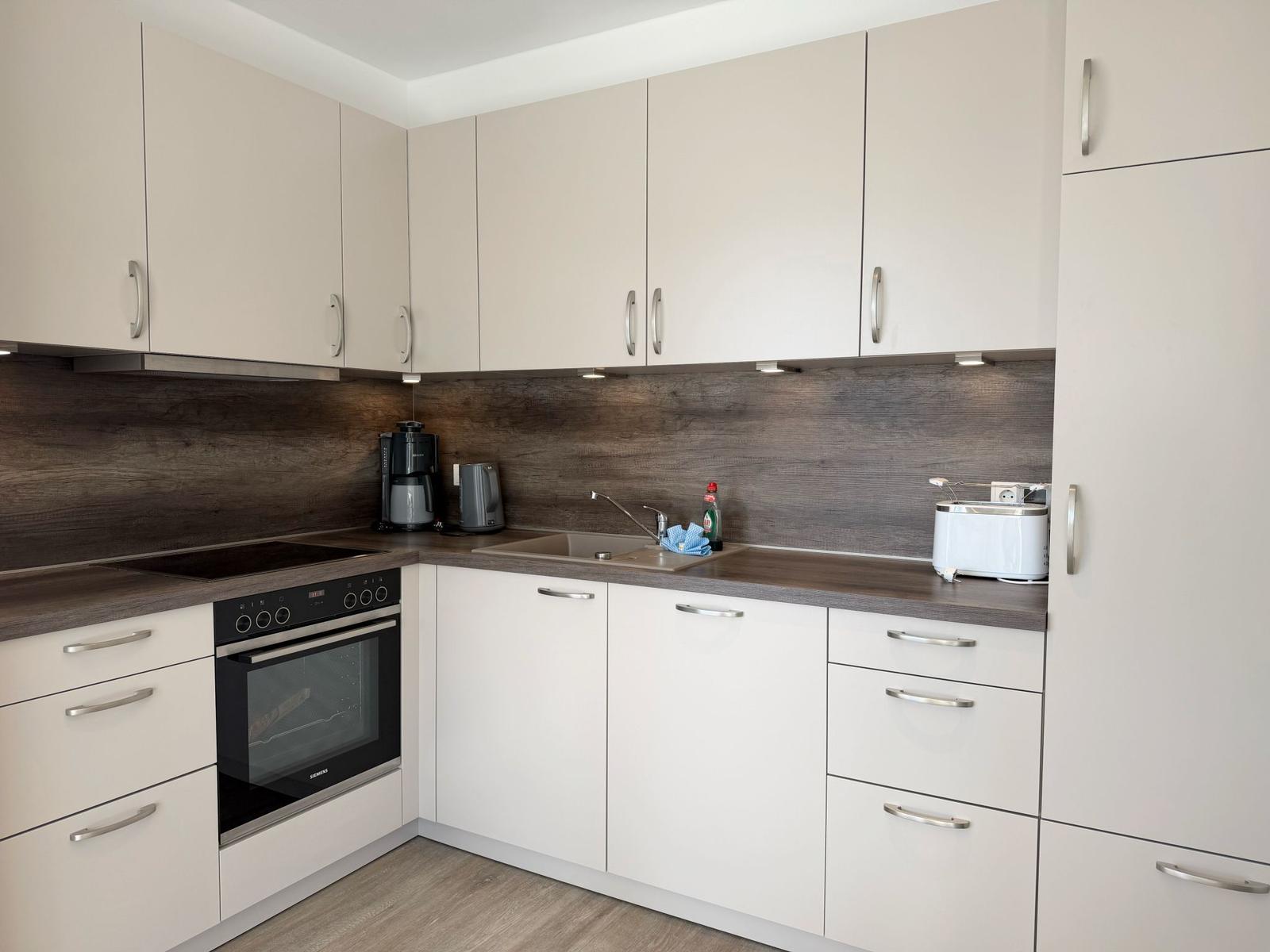 Moderne Küche mit Dunstabzug, Spüle, Herd und Kühlschrank.