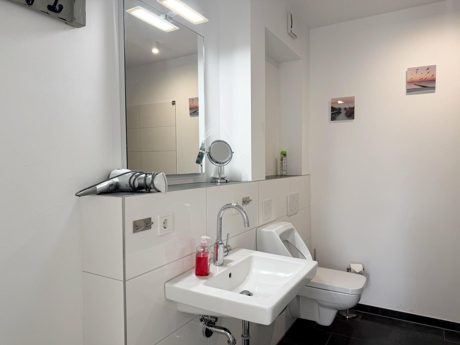 Badezimmer mit Waschbecken, Spiegel, Toilette und Urinal.