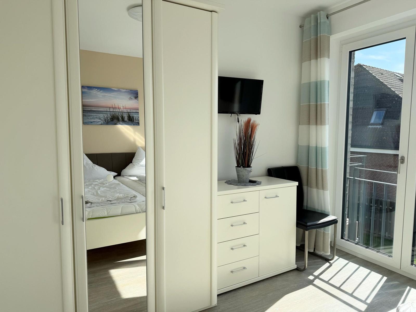 Schlafzimmer mit Doppelbett, Schrank und TV. Balkon mit Blick auf Gebäude.