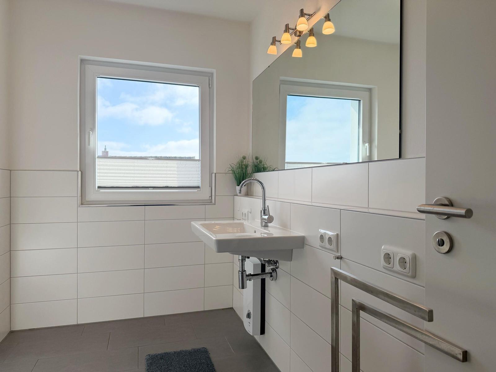Badezimmer mit Waschbecken, Spiegel und Fenster mit Blick auf Dach.