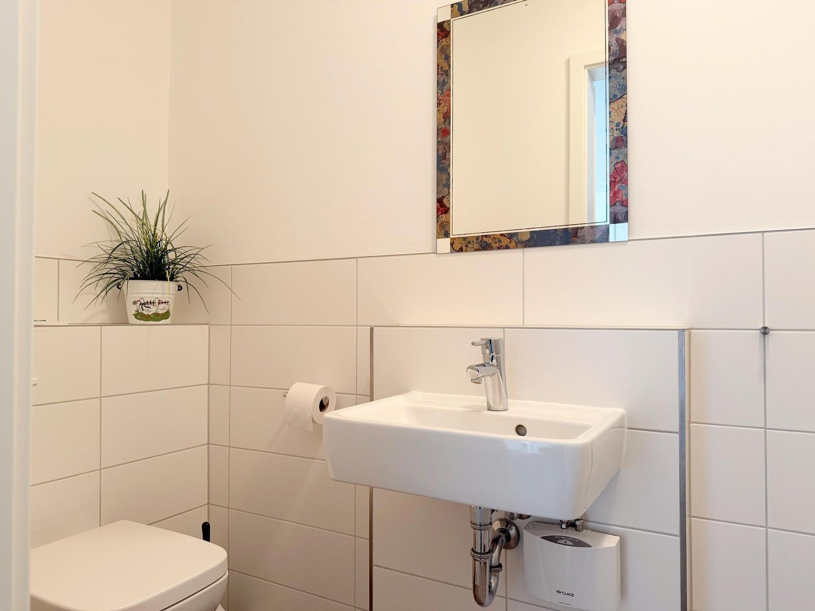 Badezimmer mit Waschbecken, Spiegel, Toilette und Pflanze.
