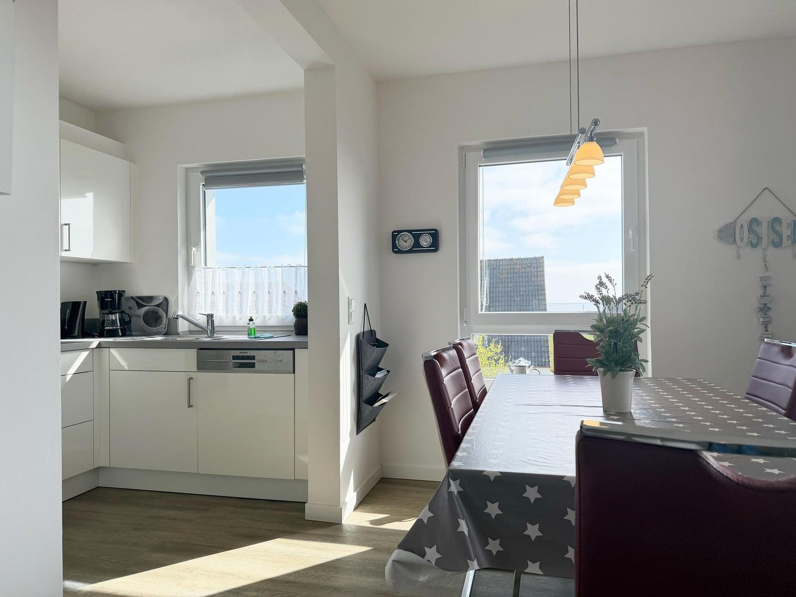 Esszimmer mit Tisch, Stühlen und Fenster. Küche mit Arbeitsplatte und Spüle.
