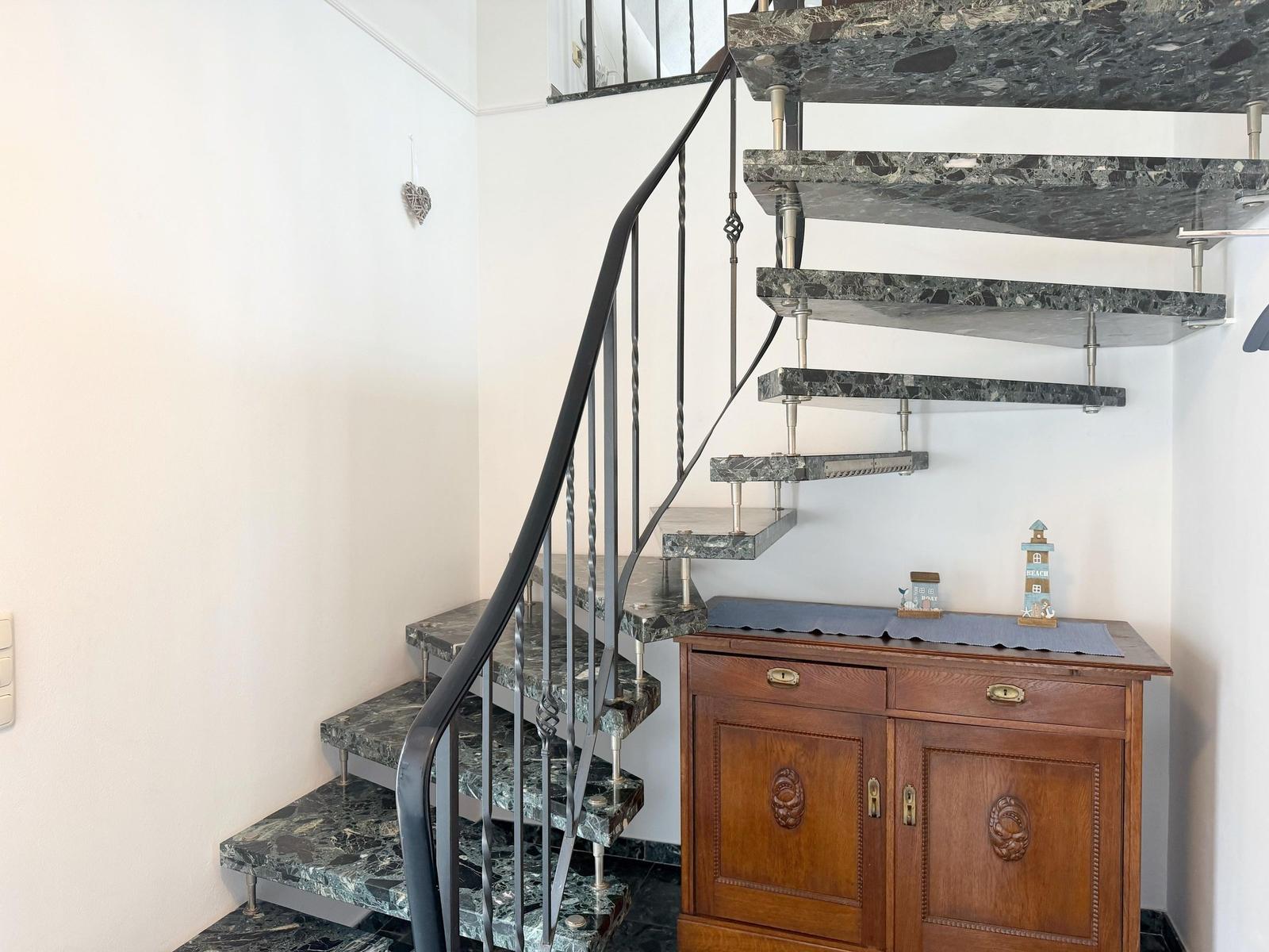 Treppe mit Marmorstufen und Metallgeländer neben einem Holzschrank mit Dekorationsgegenständen.
