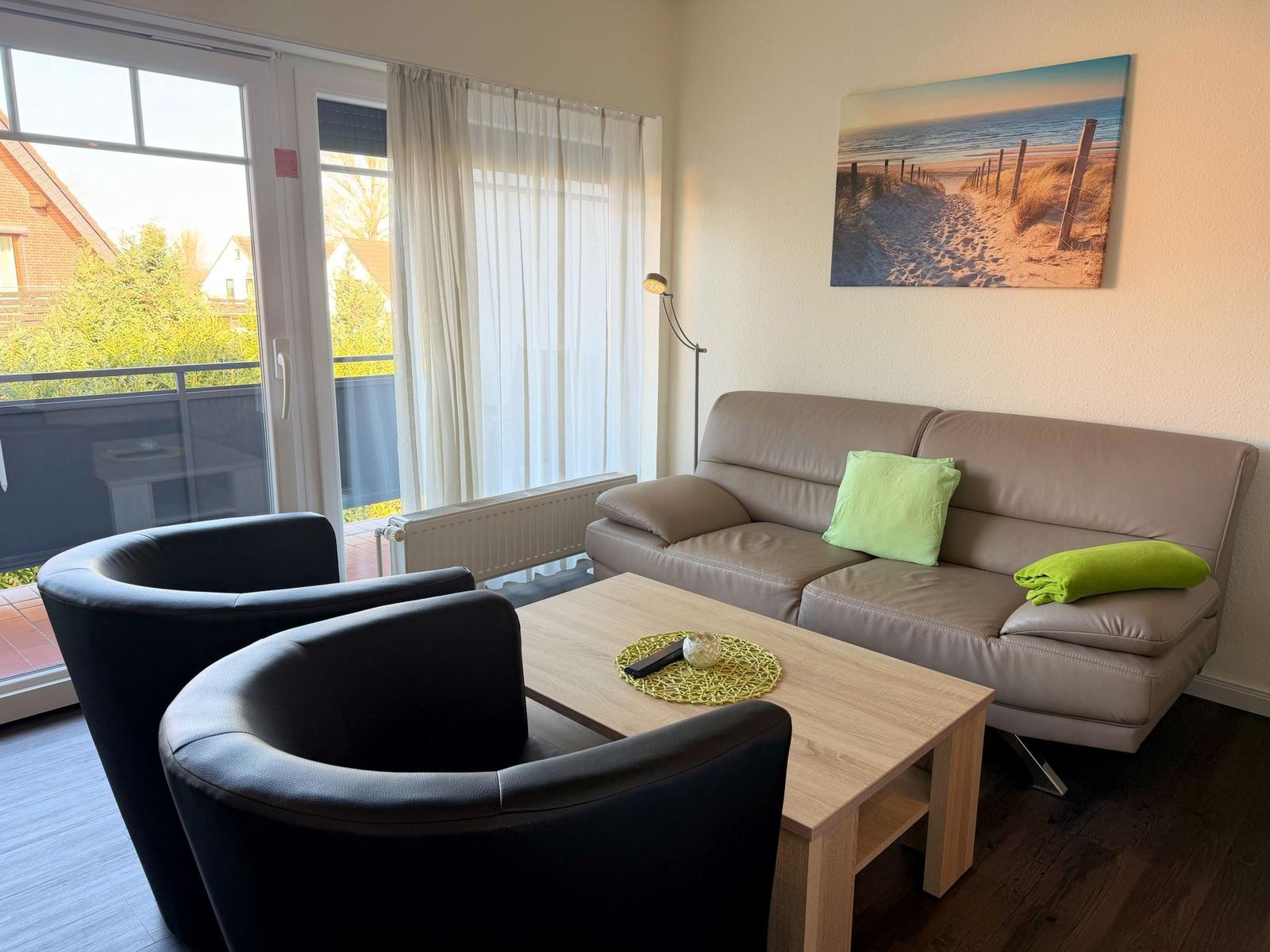 Wohnzimmer mit Sofa, zwei Sesseln und Tisch. An der Wand hängt ein Strandbild.